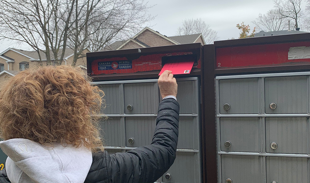 Rachel placing a red envelope into a mailbox.