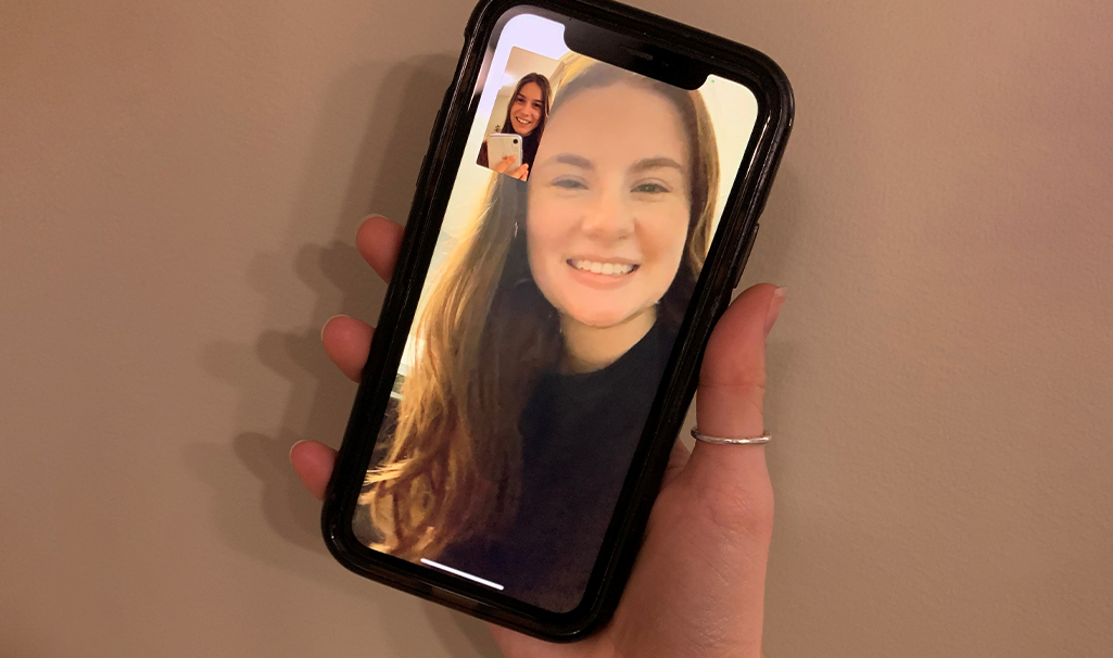 A woman holds a phone featuring a girl's photo as two women connect through a FaceTime video call.