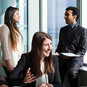 Rachel Bierbrier smiles while speaking at a table, with two colleagues behind her.