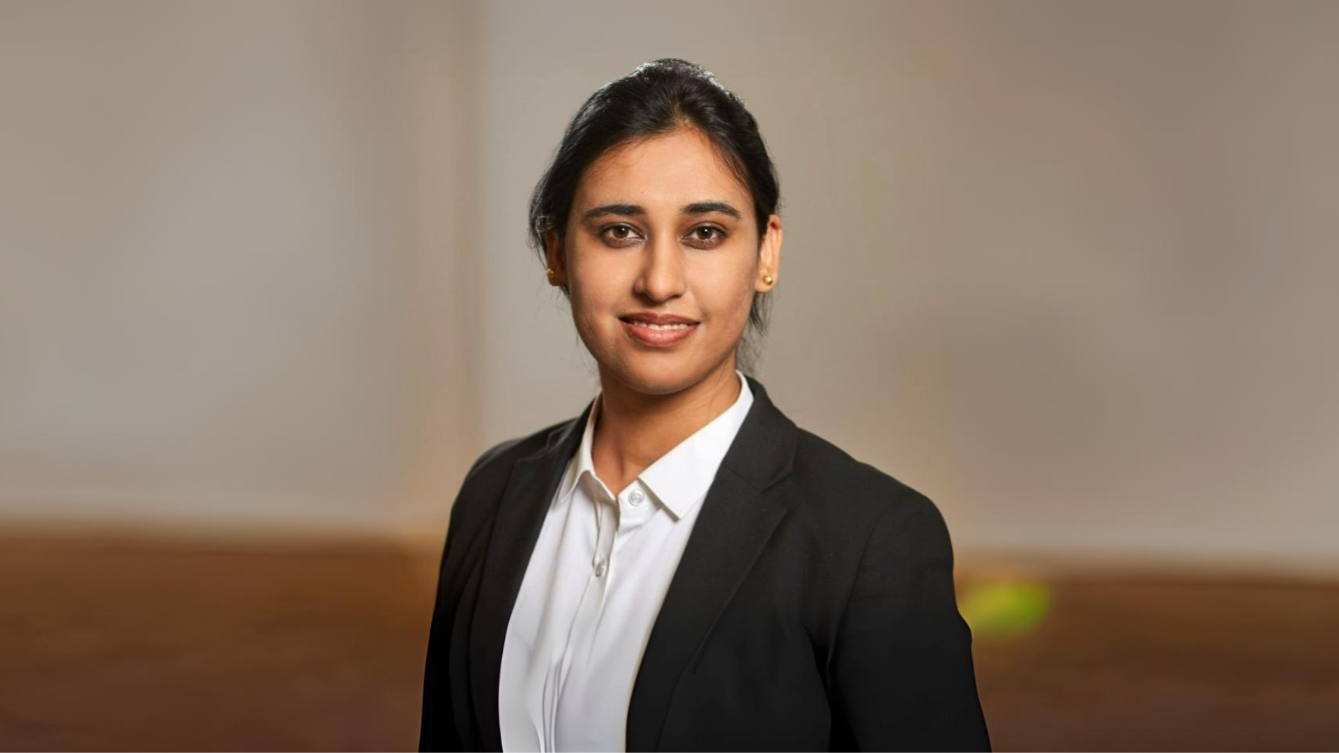 Shweta Sapra, a woman in a business suit and tie, smiles warmly.