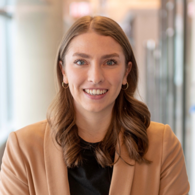 A smiling woman named Sydney Van Sickle wearing a tan blazer over a black shirt.