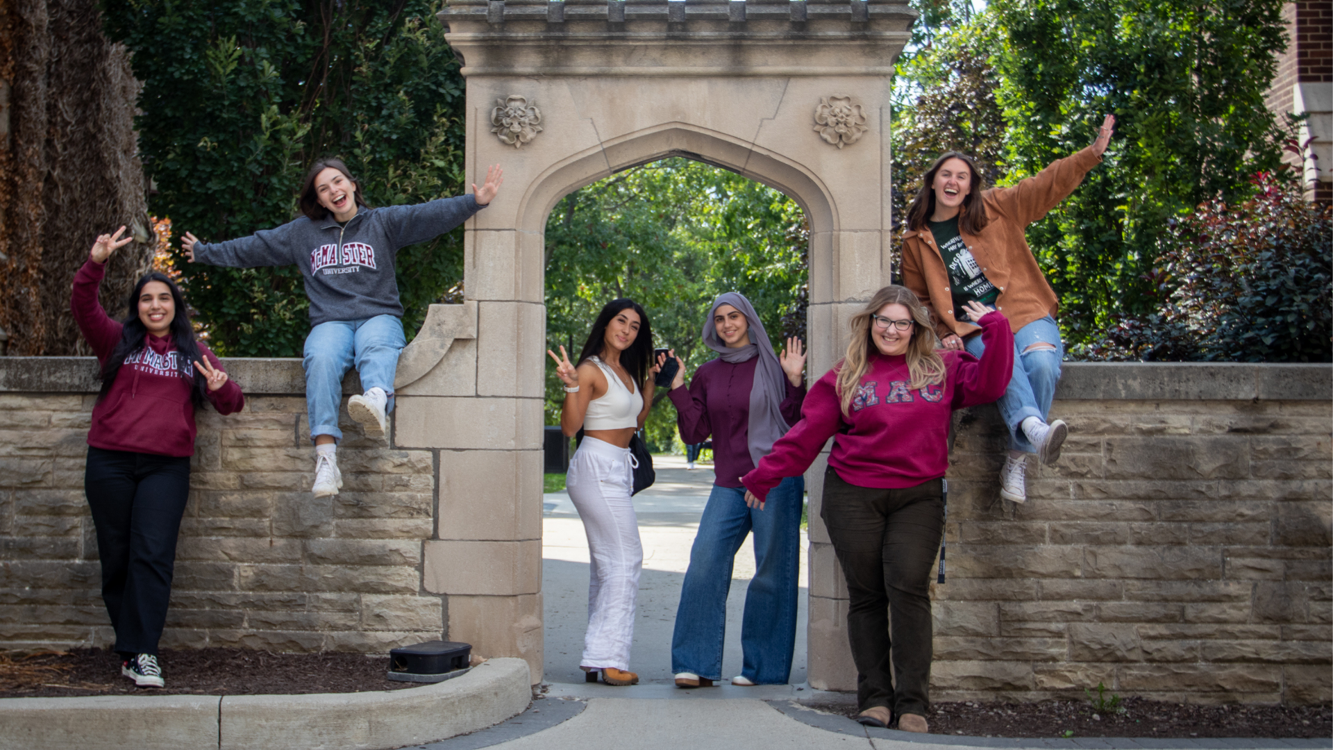 Six DeGroote female students smiling and posing in front of the Edwards Arch at McMaster Main Campus.