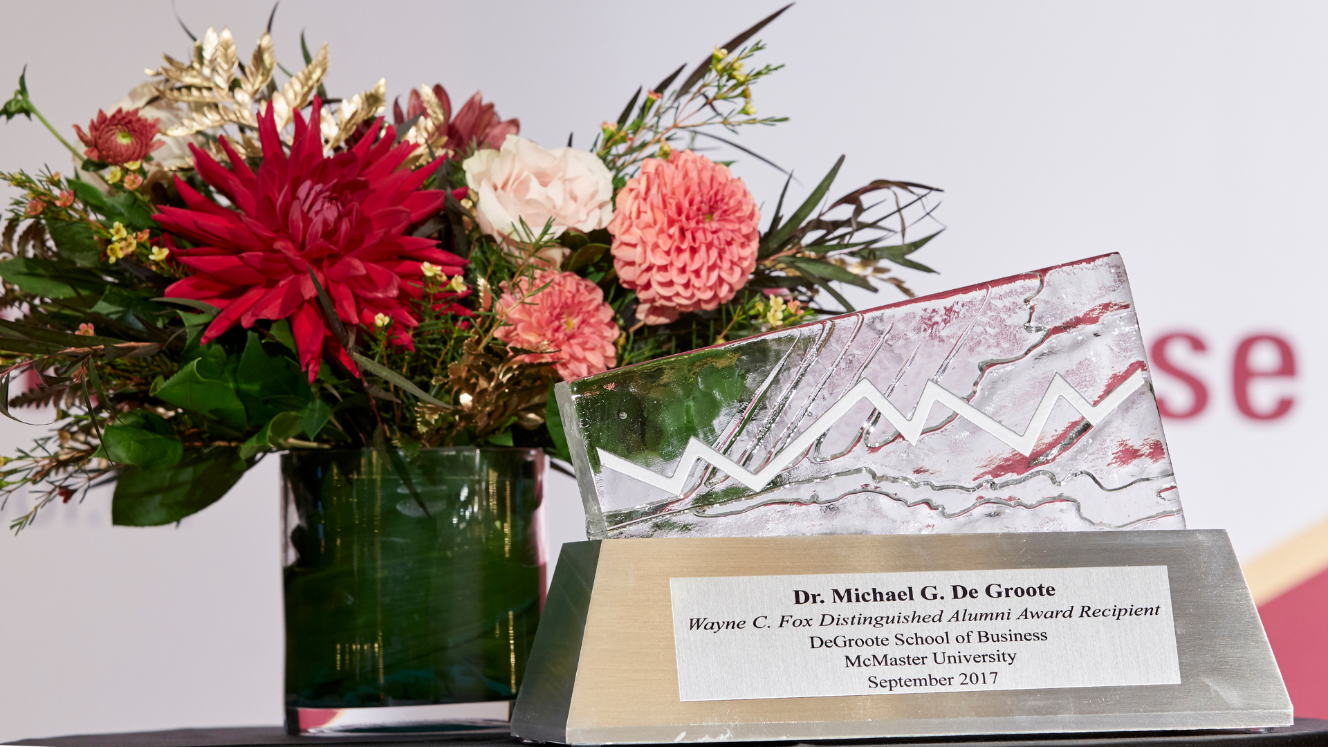 A close-up of a glass trophy with a plaque, surrounded by flowers in a vase on a table.