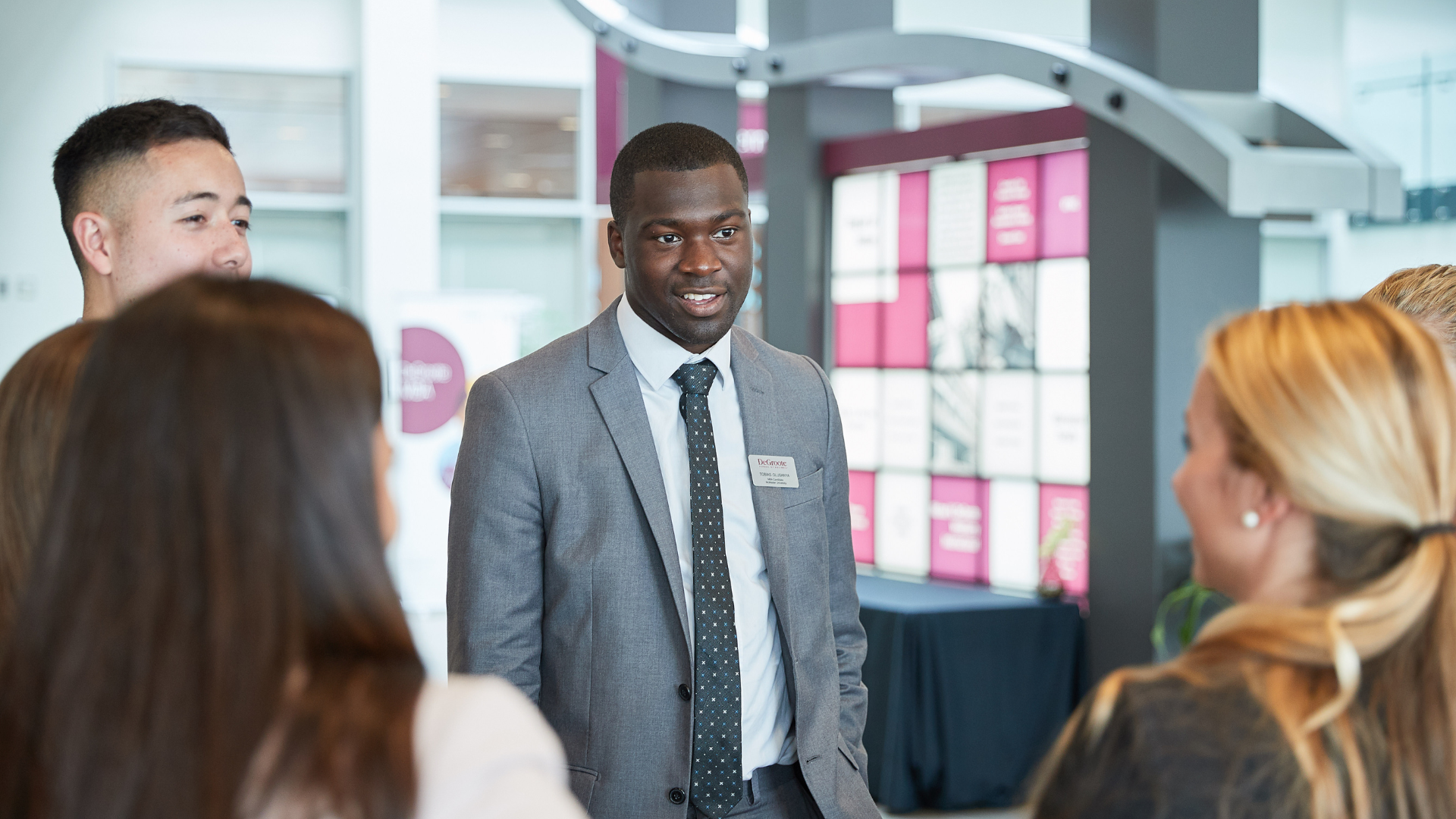 DeGroote candidate recruiter in a suit converses with a group of students.