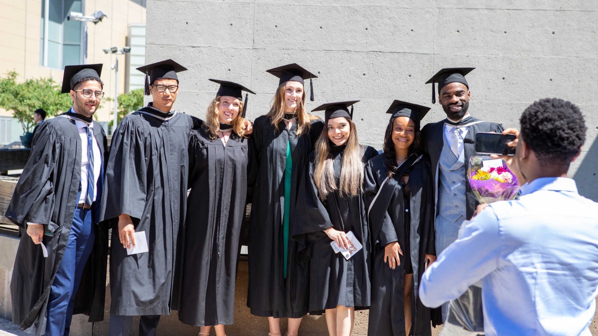 A group of DeGroote graduates in caps and gowns poses together for a celebratory photo.