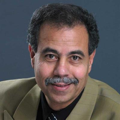 Mohamed Shehata, a man with a mustache, dressed in a suit jacket, smiling warmly at the camera.