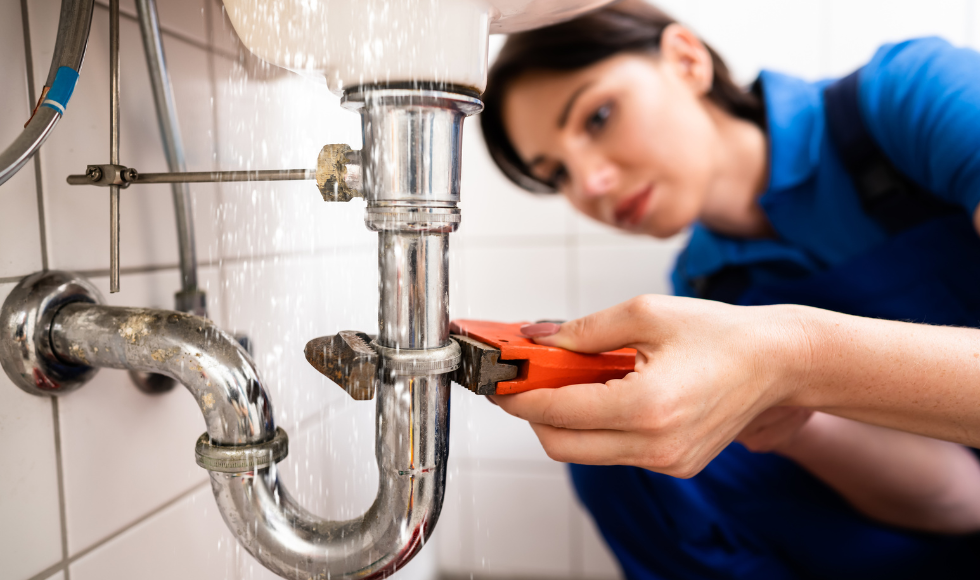 A woman uses a wrench to repair a pipe, demonstrating practical skills in plumbing maintenance.