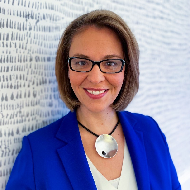 Meaghan Stovel-McKnight, a woman in glasses and a blue blazer, smiles warmly