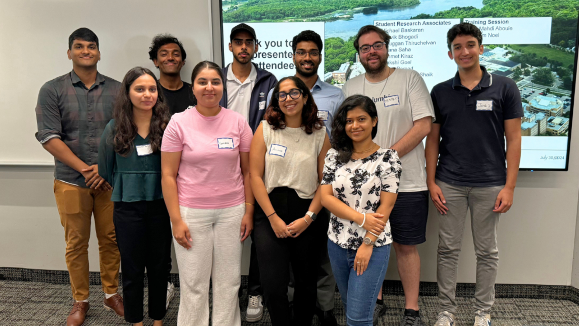 A group of student researchers smiles for a photo in front of a projector screen.