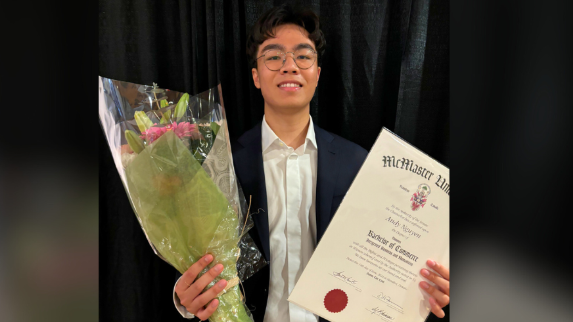 IBH student at convocation holding his degree and flowers.