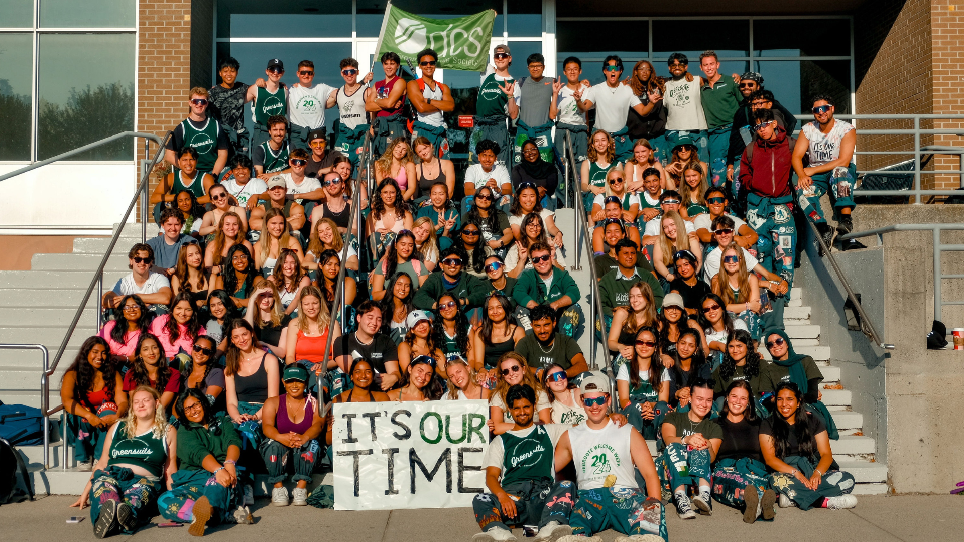 A group of DeGroote Greensuits gather in front of the DeGroote building.