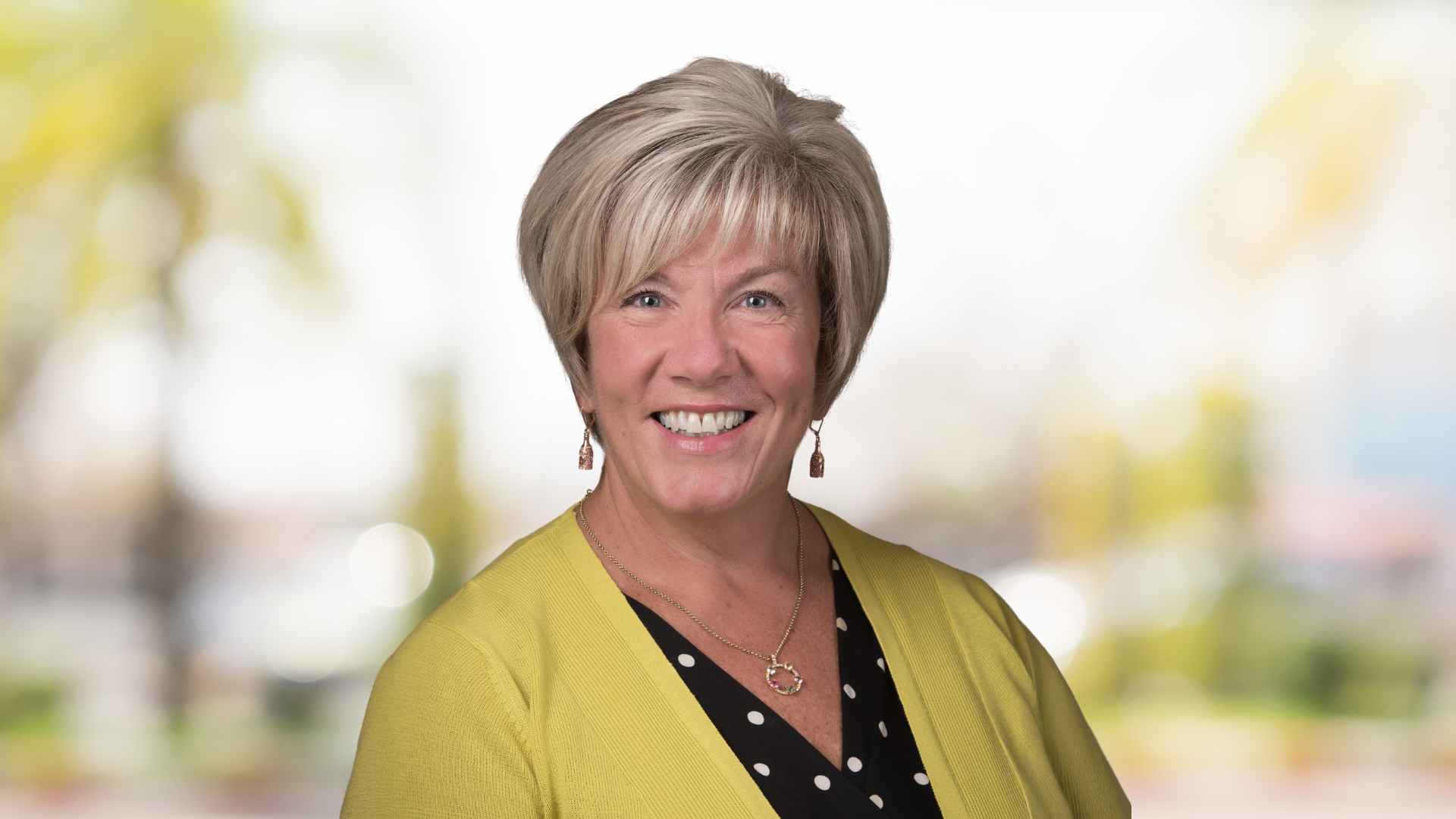 Nancy MacCready Williams, a woman with short blonde hair, smiles while dressed in a cheerful yellow cardigan.