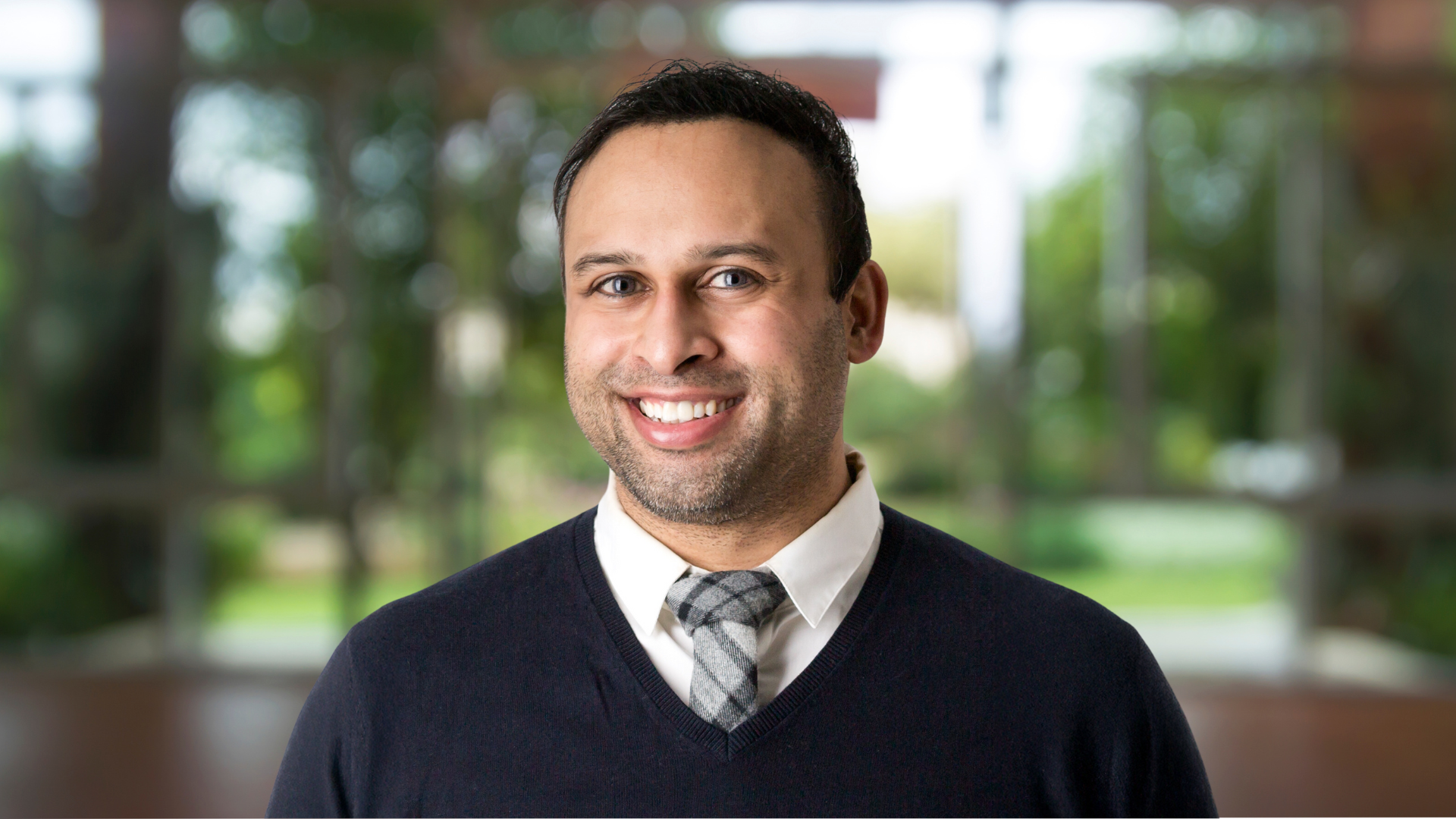 Dr. Monty Ghosh, a man in a sweater and tie, smiles warmly.