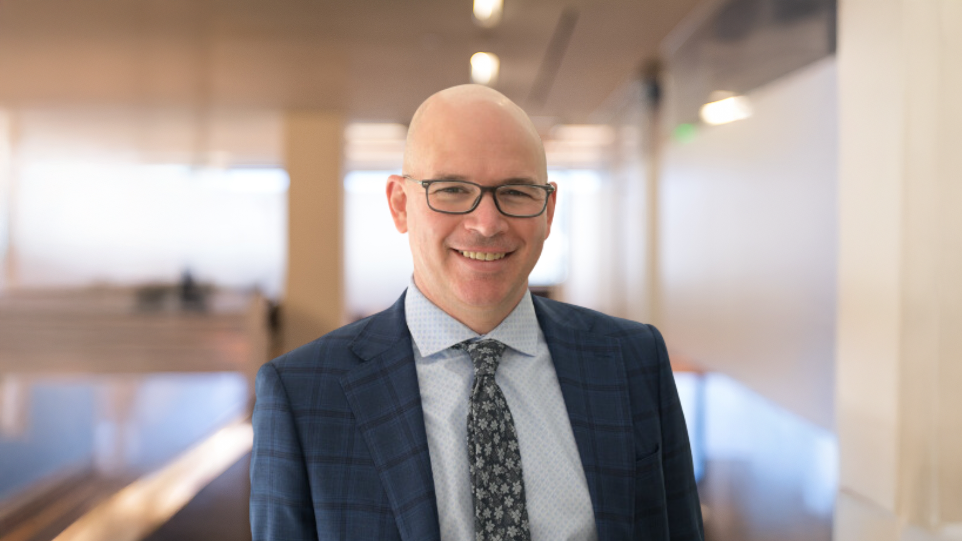 Michael Heenan, dressed in a suit and tie, displays a cheerful smile.