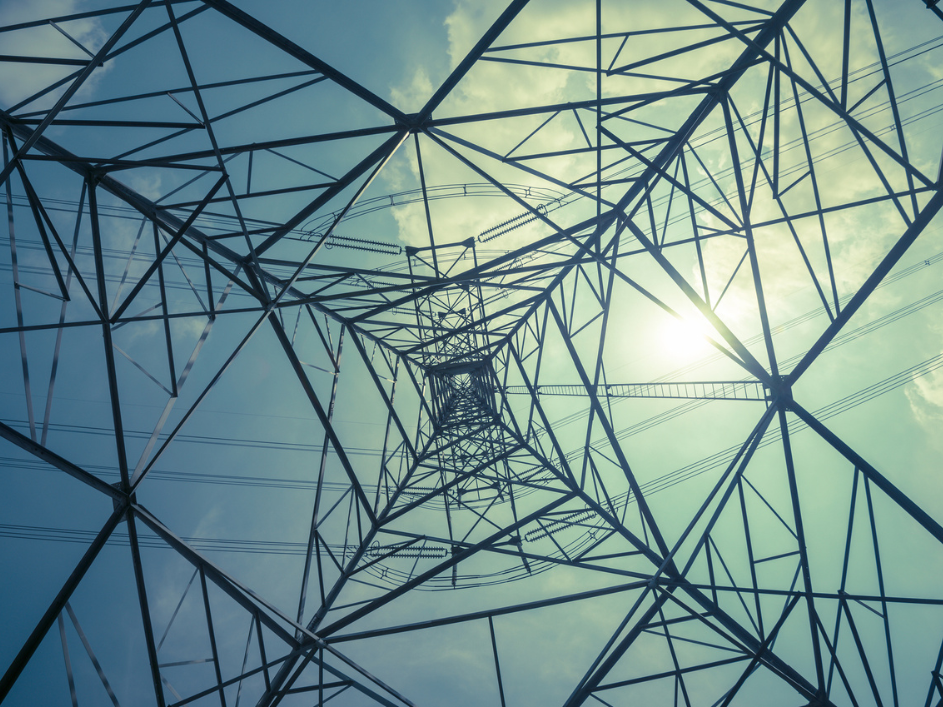 An electricity tower stands tall against the backdrop of the sun shining through.