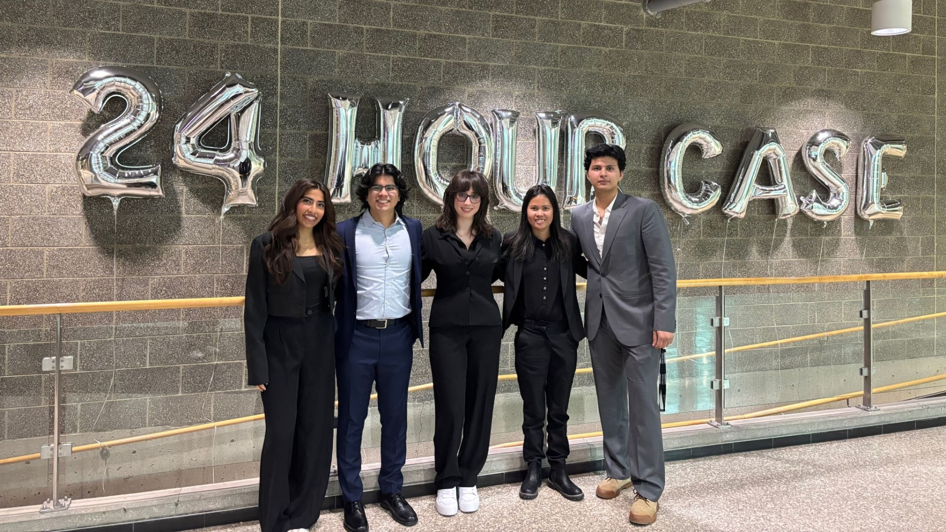 A group of five DeGroote students stand cheerfully by the 24 Hour Case sign.