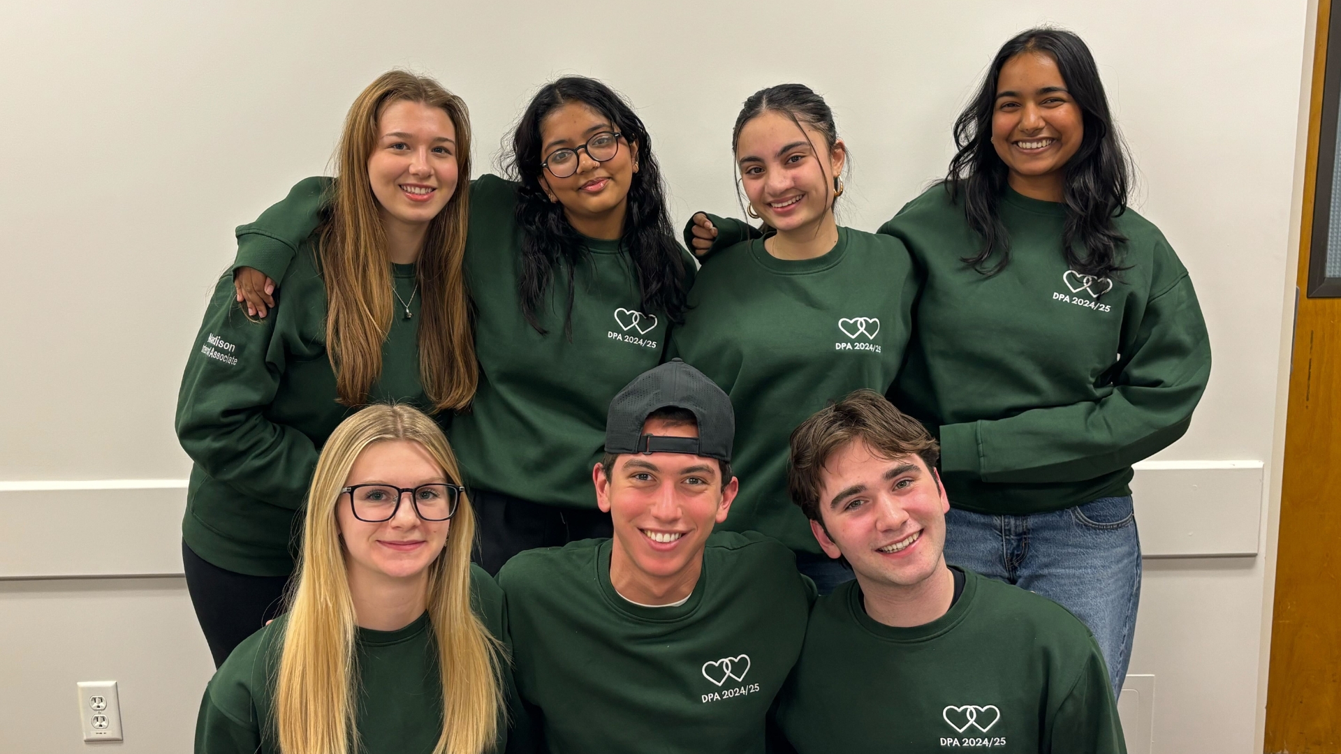 DeGroote Pride Association members, dressed in green sweatshirts, pose together with smiles.