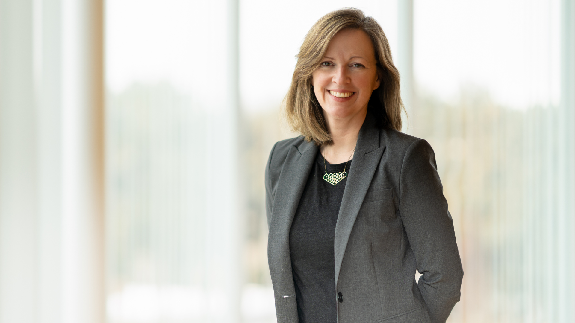 Erin Reid, dressed in a business suit, stands poised in front of a window.