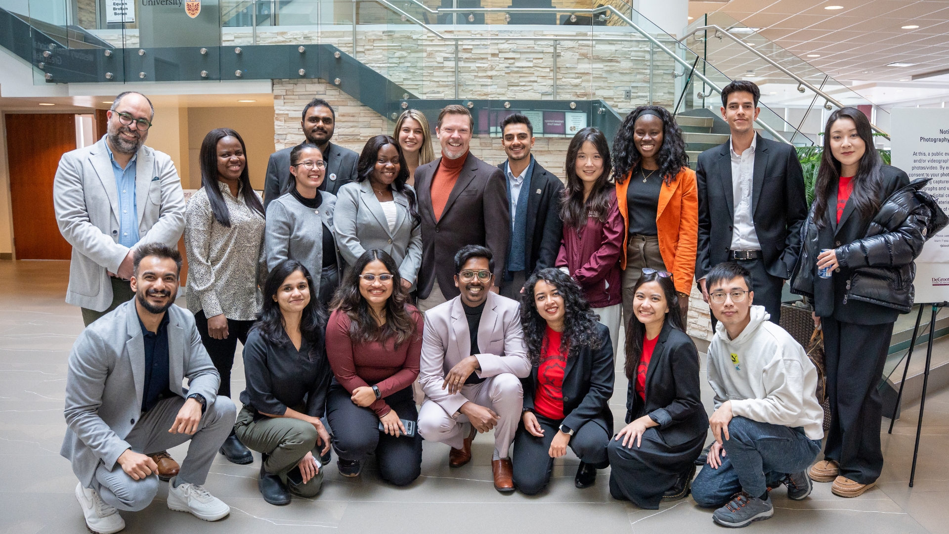 DeGroote MBA students and faculty gather for a group photo, smiling and standing close together.