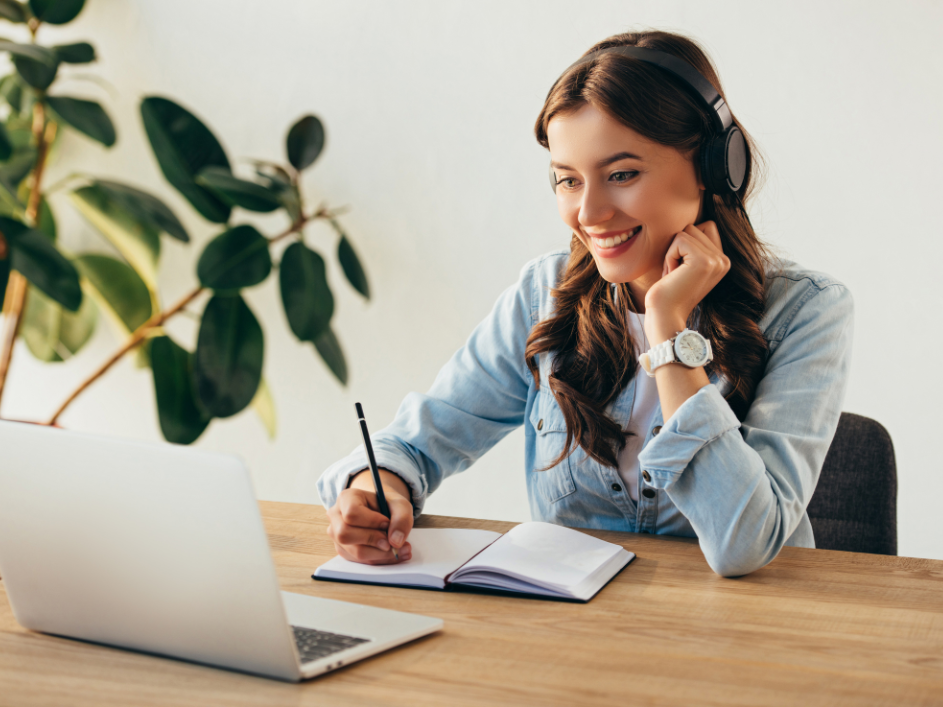 A woman smiling, getting ready to take notes as she looks at her laptop screen.