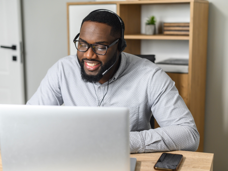 A smiling man with headphones on looking at his laptop.