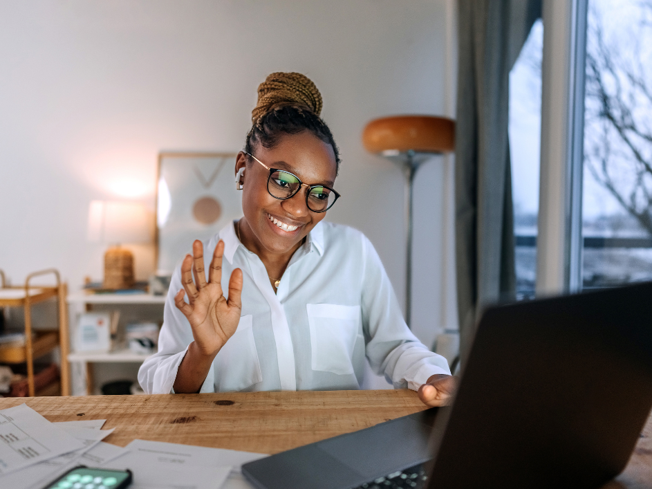 Woman smiling and waving to someone on her laptop.