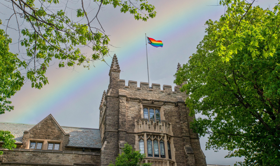University Hall flying the Pride flag with a rainbow in the background.