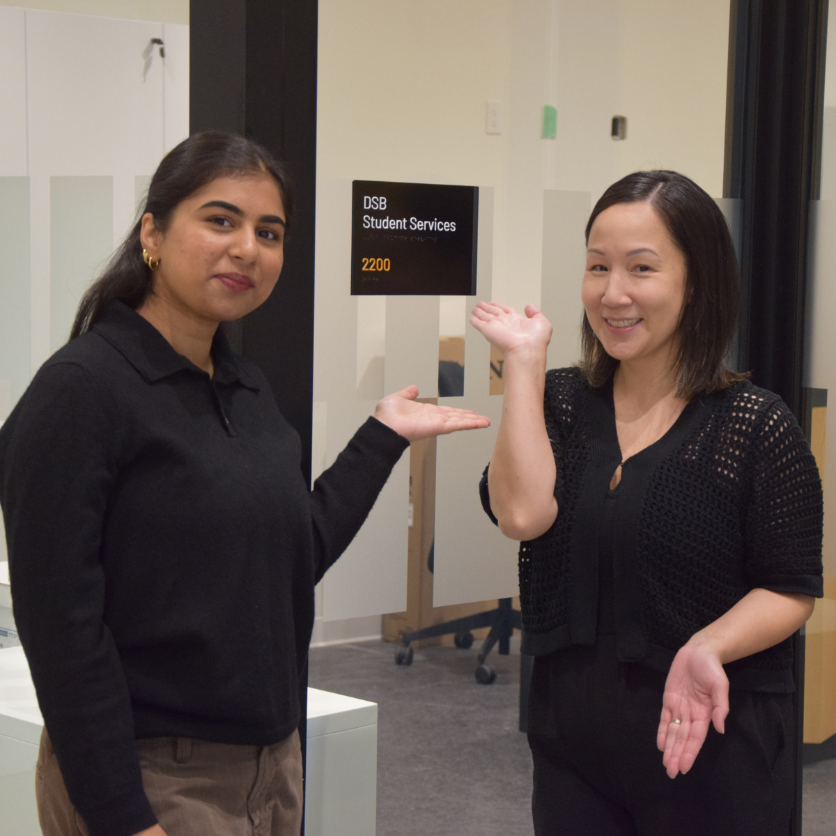Two staff members standing in front of the sign for the student services office